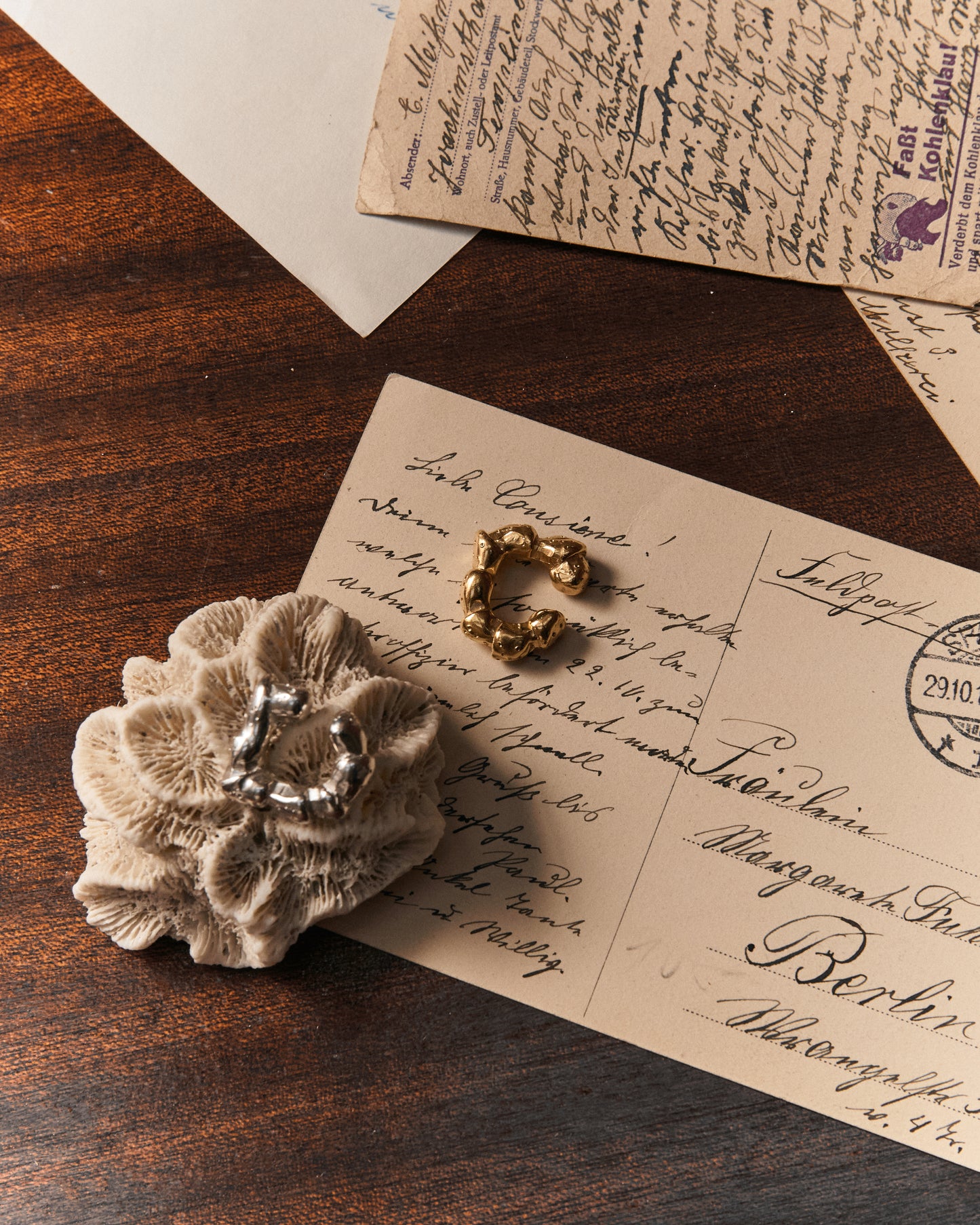 Künstlerische Produktaufnahme des Maena Ear Cuff auf einem Navigations-Tisch; Silber und gold-plattiert, Strandkrabben-Laufbein