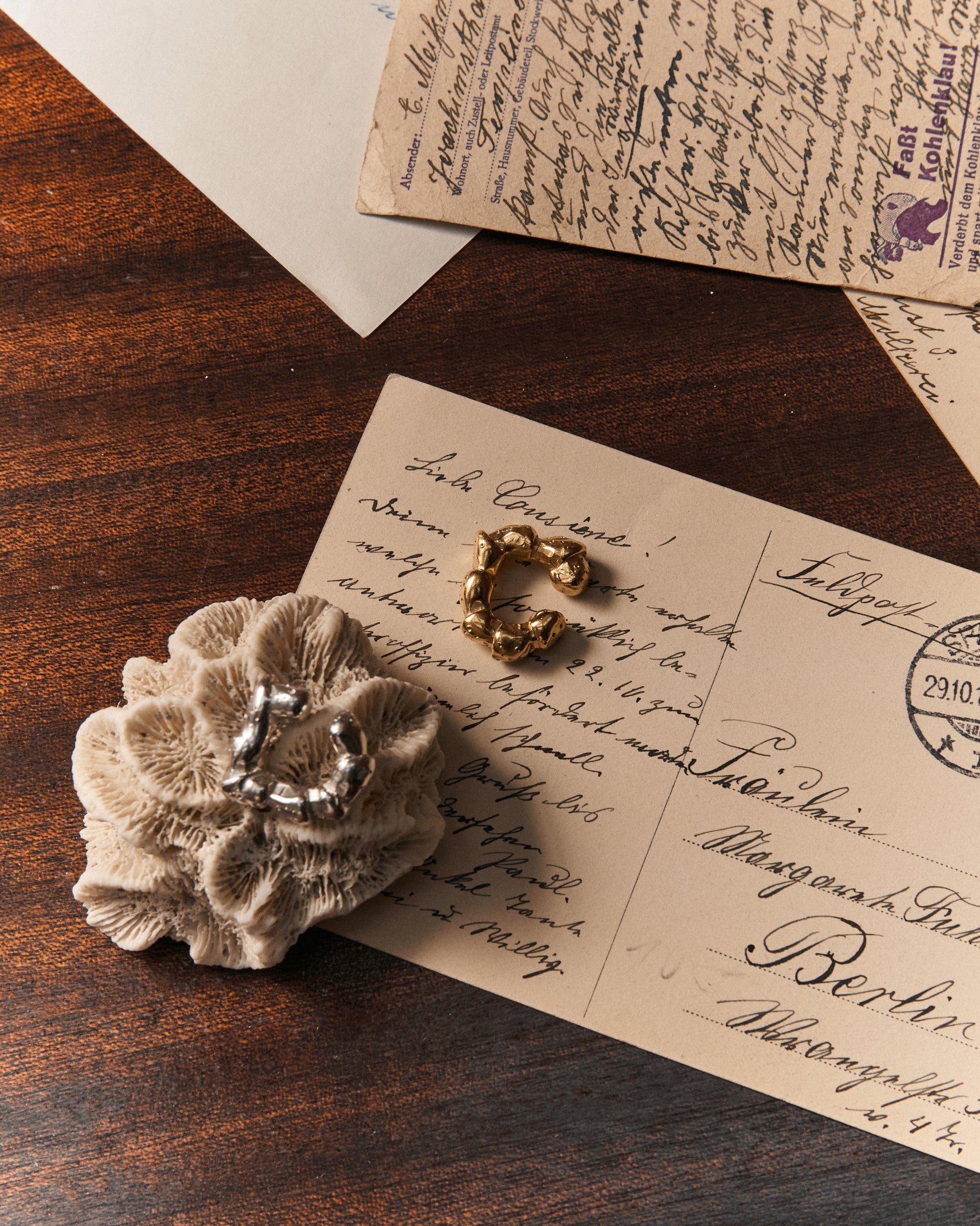 Künstlerische Produktaufnahme des Maena Ear Cuff auf einem Navigations-Tisch; Silber und gold-plattiert, Strandkrabben-Laufbein